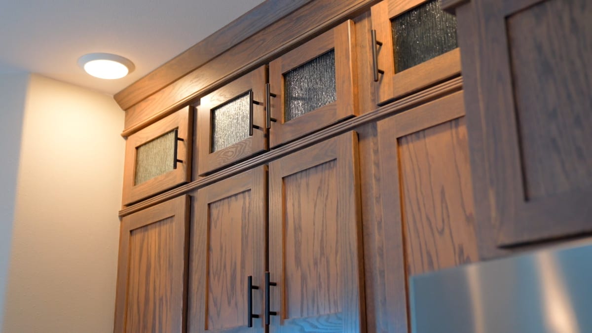 Custom wood kitchen cabinets by Wisconsin Homes with decorative glass inserts and modern black handles.