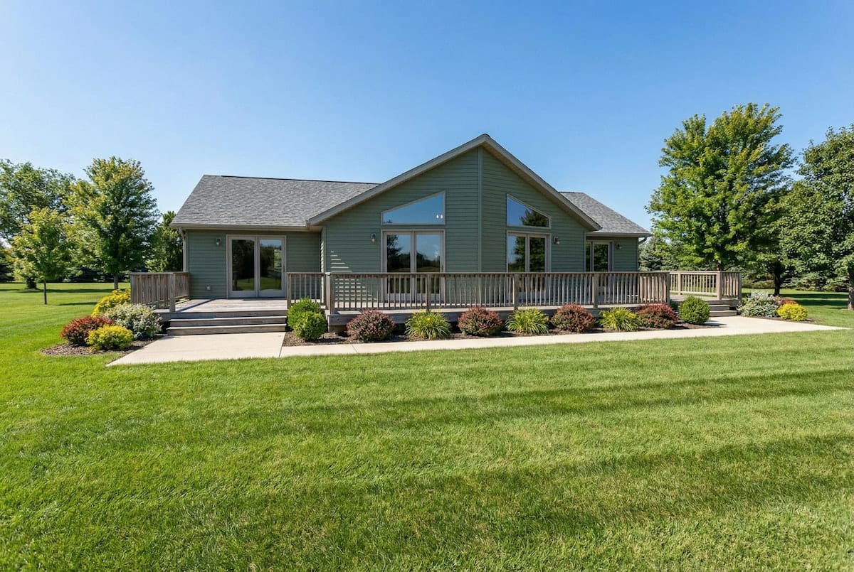 Green cottage-style modular home by Wisconsin Homes in Marshfield, WI with expansive front deck and concrete walkway.
