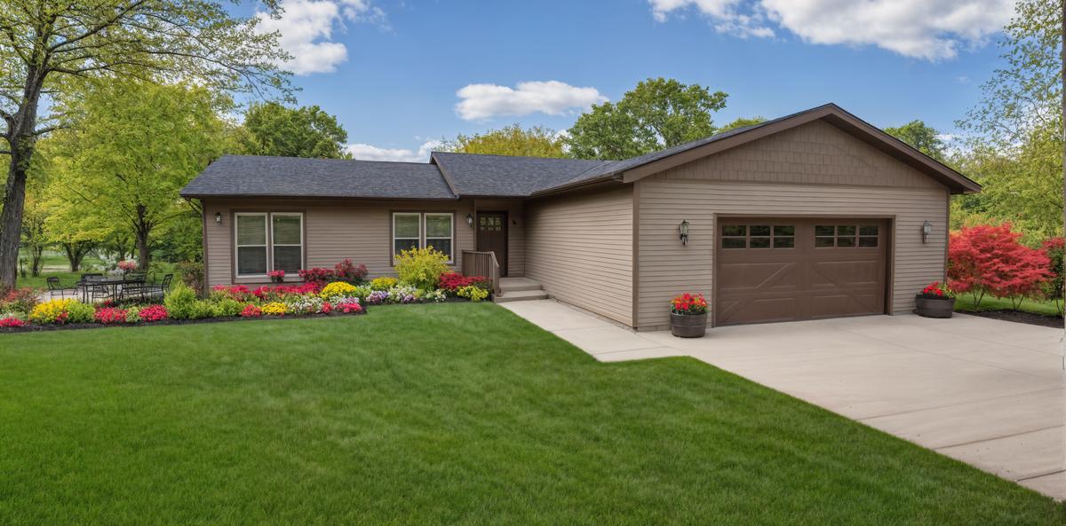 Tan cottage home by Wisconsin Homes with brown garage door, colorful landscaping, and concrete driveway.