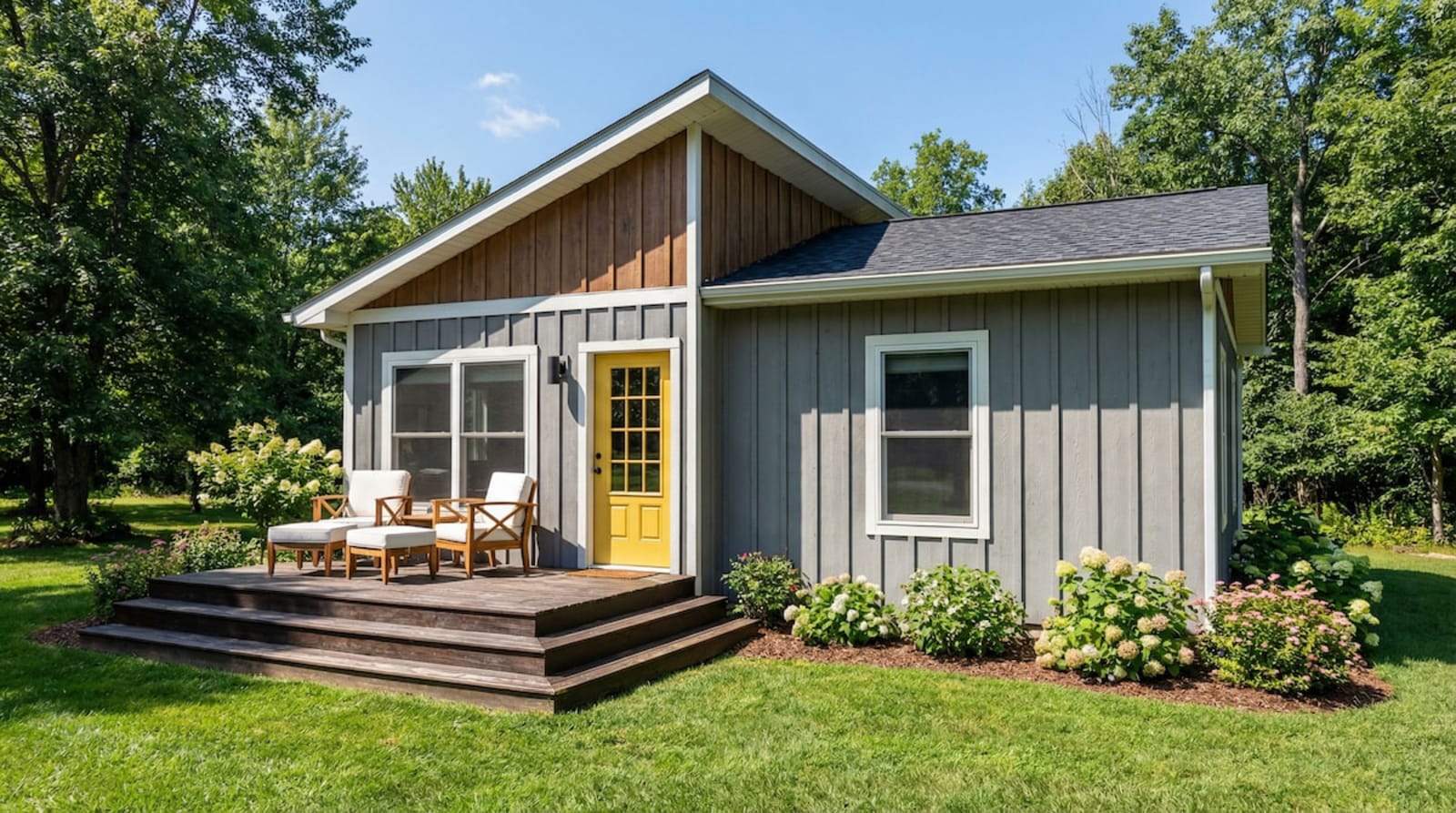 Gray cottage-style modular home by Wisconsin Homes in Marshfield, WI featuring board-and-batten siding, a yellow front door, wood gable accent, and cozy front deck with outdoor seating.