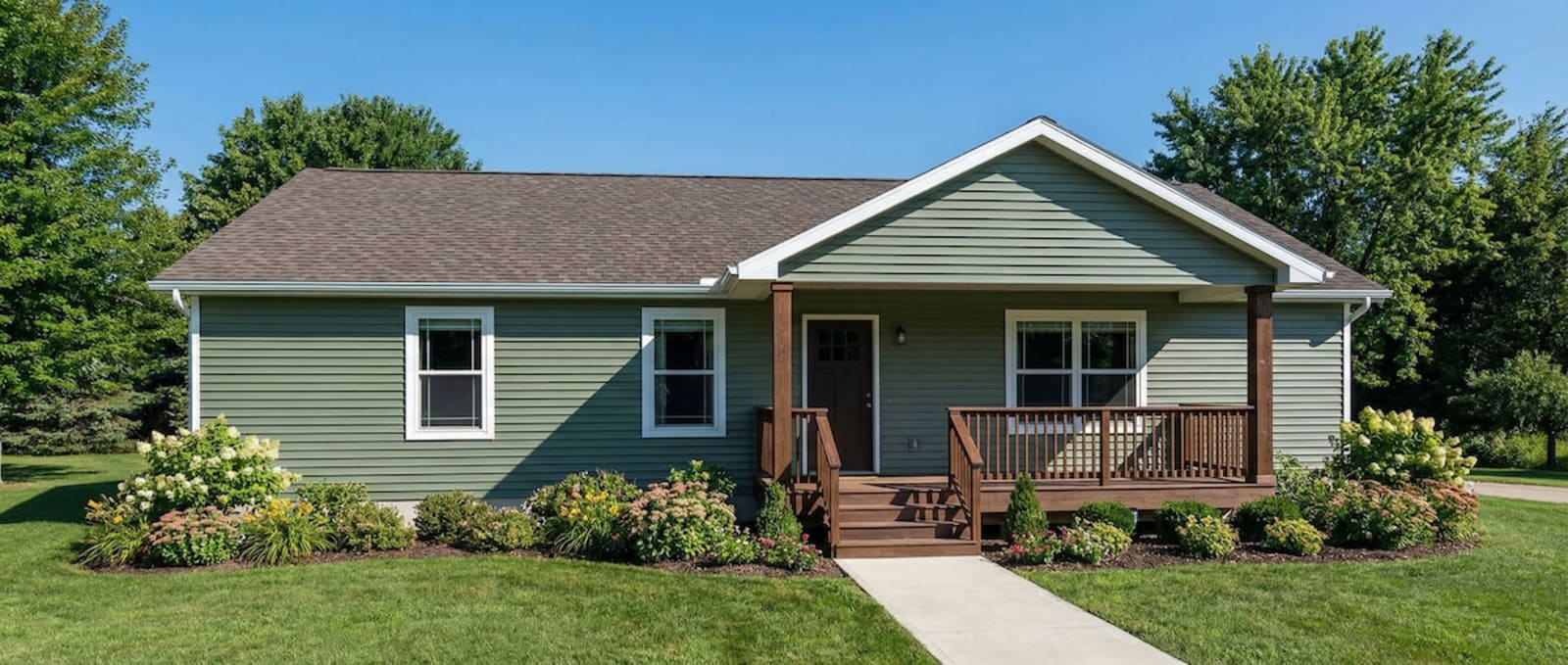Green cottage-style modular home by Wisconsin Homes in Marshfield, WI with covered front porch and landscaped yard.
