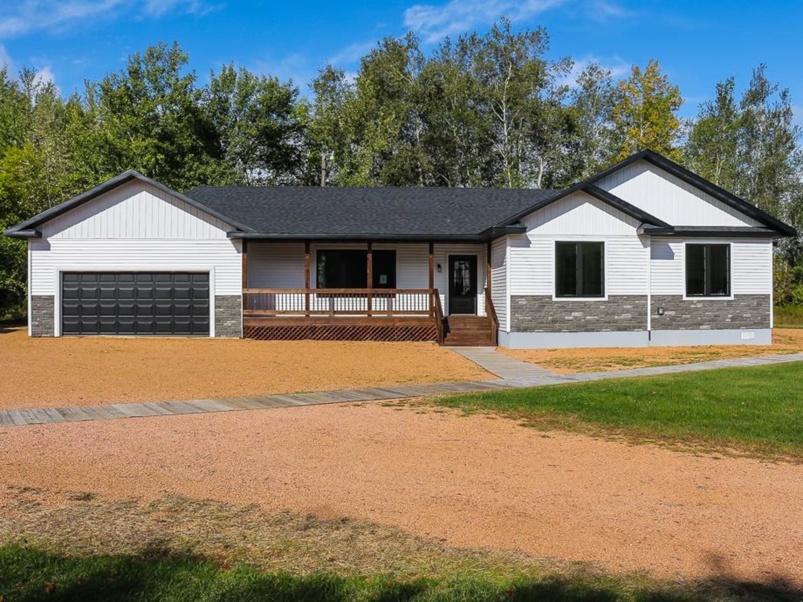 Modern white ranch-style home with black trim, large black windows, a covered porch, stone accents, and colorful front landscaping on a well-kept lawn.