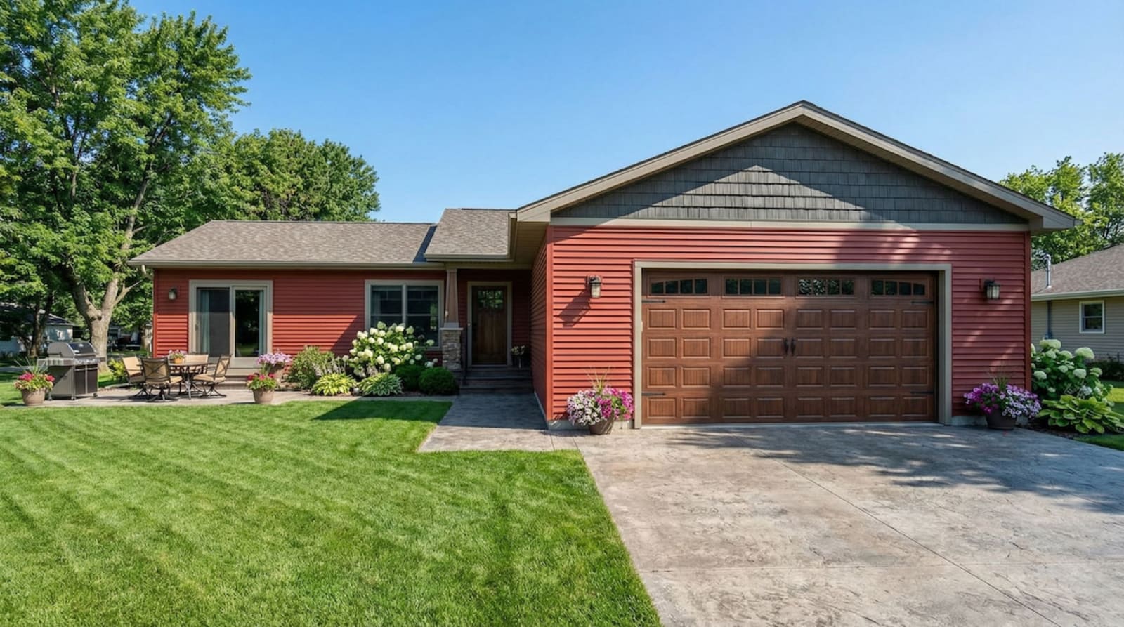 Red cottage-style modular home by Wisconsin Homes in Marshfield, WI with wood garage door and backyard patio.