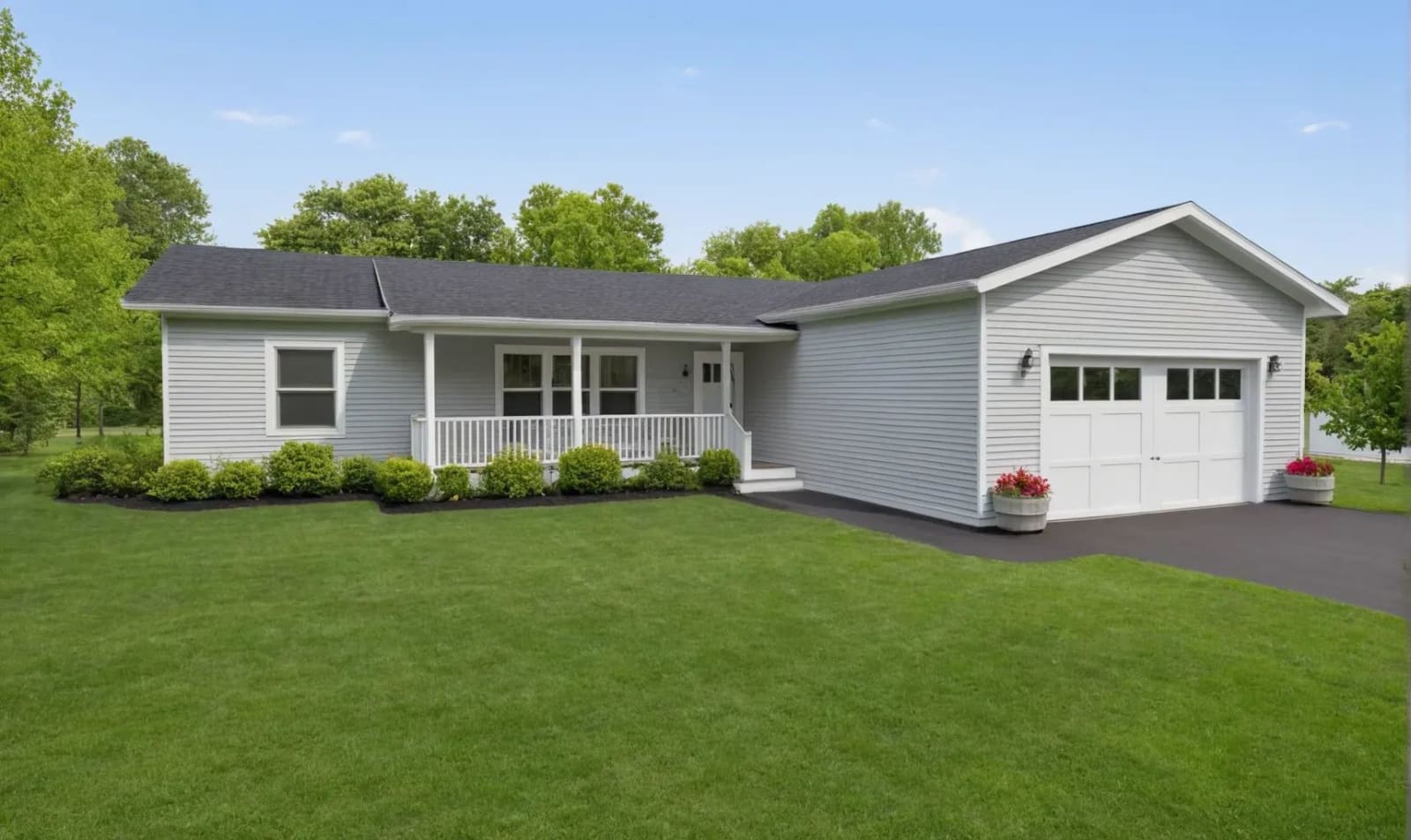 White single-story ranch-style home with black roof, attached one-car garage, covered front porch, and neatly trimmed shrubs on a large green lawn.