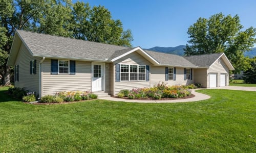 Beige modular ranch home with blue shutters, attached garage, and flower landscaping by Wisconsin Homes in Marshfield, WI.