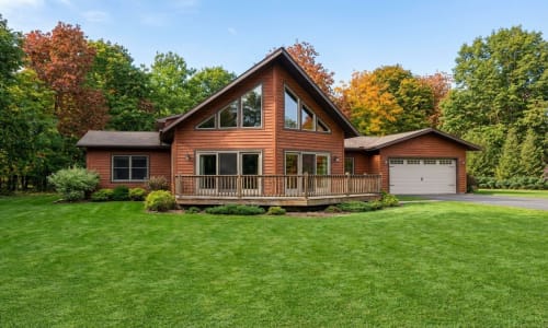 Cedar-toned Chalet-style modular home by Wisconsin Homes in Marshfield, WI with large windows and attached garage.