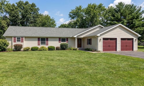 Single-story modular ranch home by Wisconsin Homes with tan siding and red garage doors in Marshfield, WI.