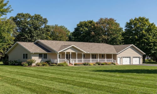 Tan modular ranch home by Wisconsin Homes featuring a wraparound front porch and attached two-car garage in Marshfield, WI.