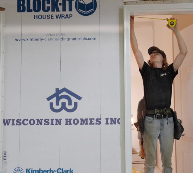 Construction worker measuring door frame at Wisconsin Homes build site with BLOCK-IT house wrap visible.