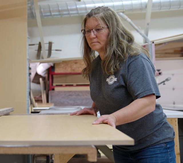 Wisconsin Homes factory worker inspecting wood panel for quality in custom home manufacturing shop.