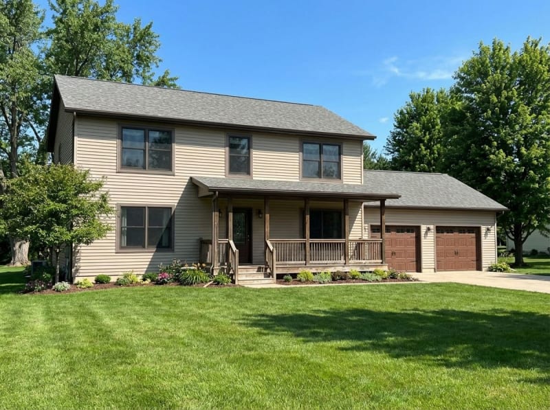 Tan Colonial-style modular home by Wisconsin Homes in Marshfield, WI with covered front porch and two-car garage.