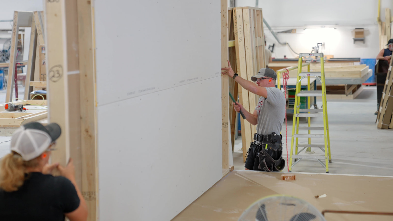 Construction team installing drywall panels during modular home assembly at Wisconsin Homes facility.