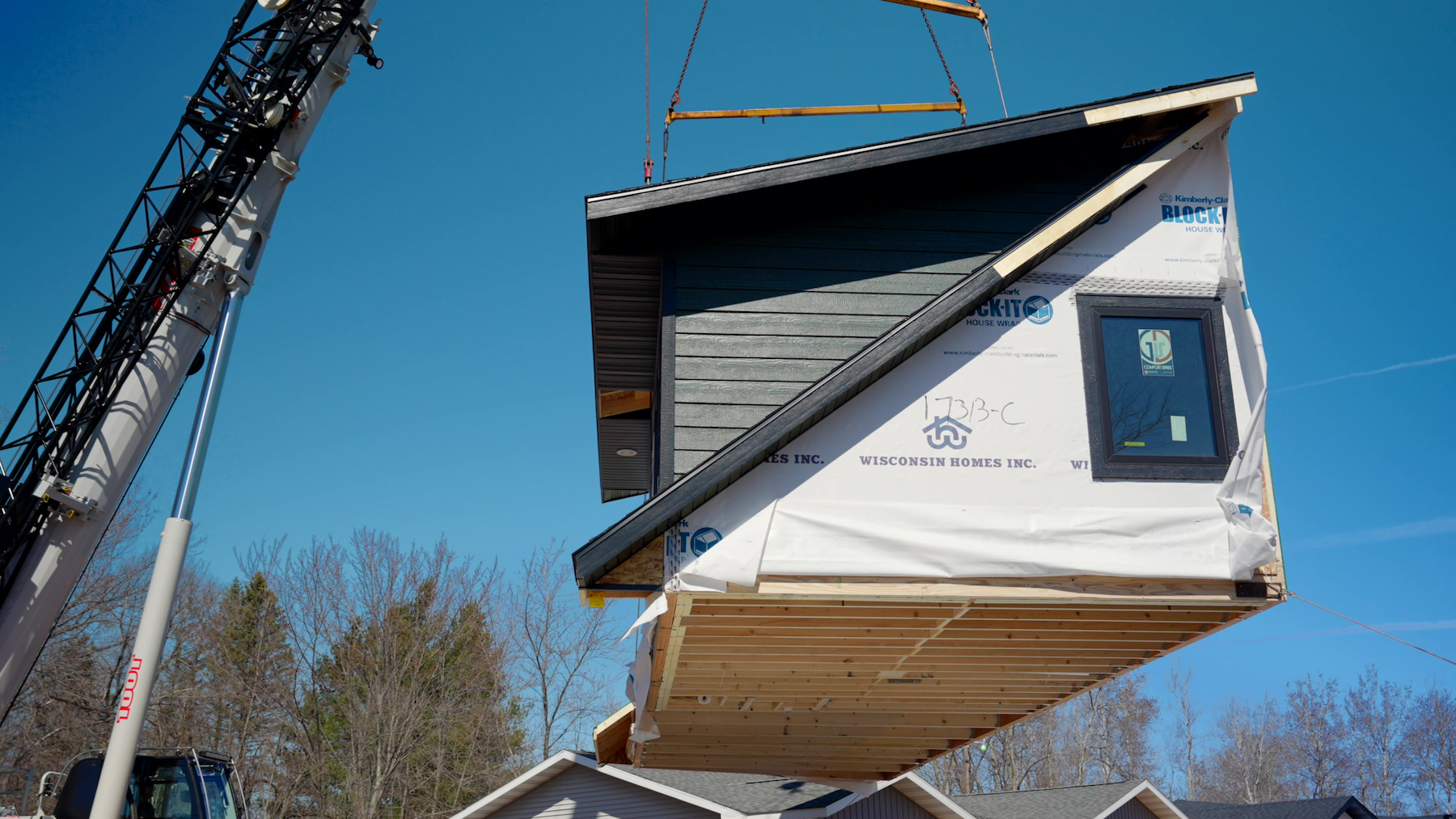Crane hoisting modular home section wrapped in Block-It during on-site installation by Wisconsin Homes.