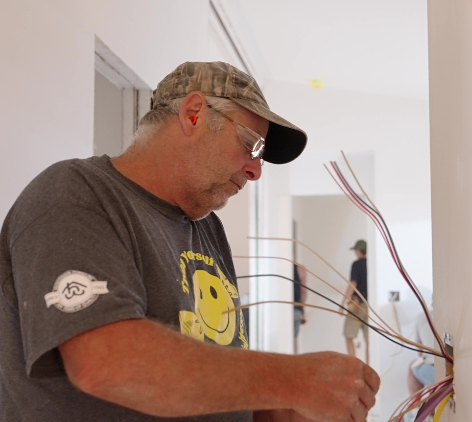 Electrician at Wisconsin Homes installing electrical wiring in new home with safety glasses and ear protection.