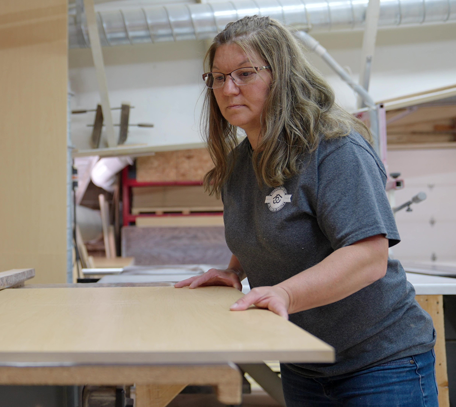 Wisconsin Homes factory worker inspecting wood panel for quality in custom home manufacturing shop.
