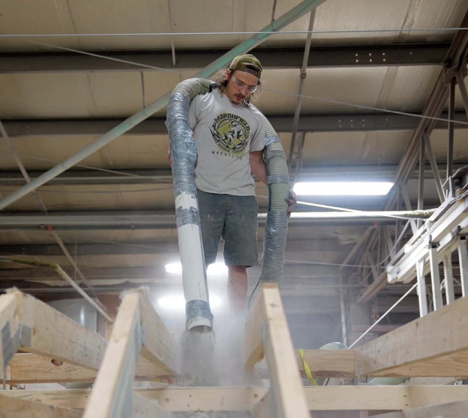 Wisconsin Homes worker installing insulation into floor system at factory using large hose equipment.