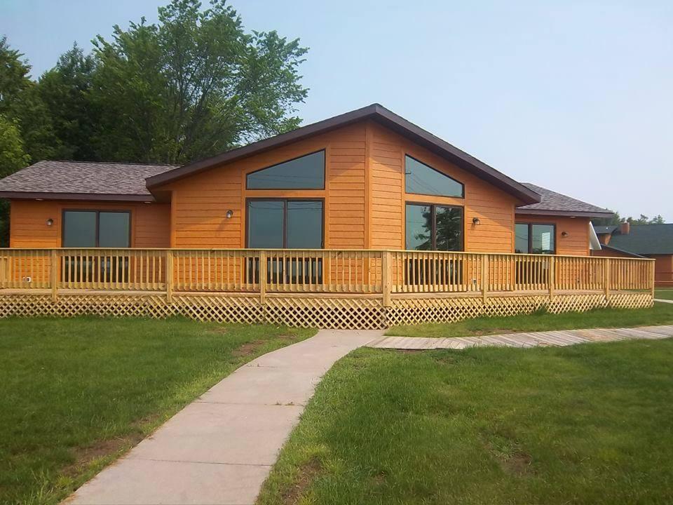 Cedar cottage-style home by Wisconsin Homes with a wraparound wood deck, large windows, and manicured lawn.