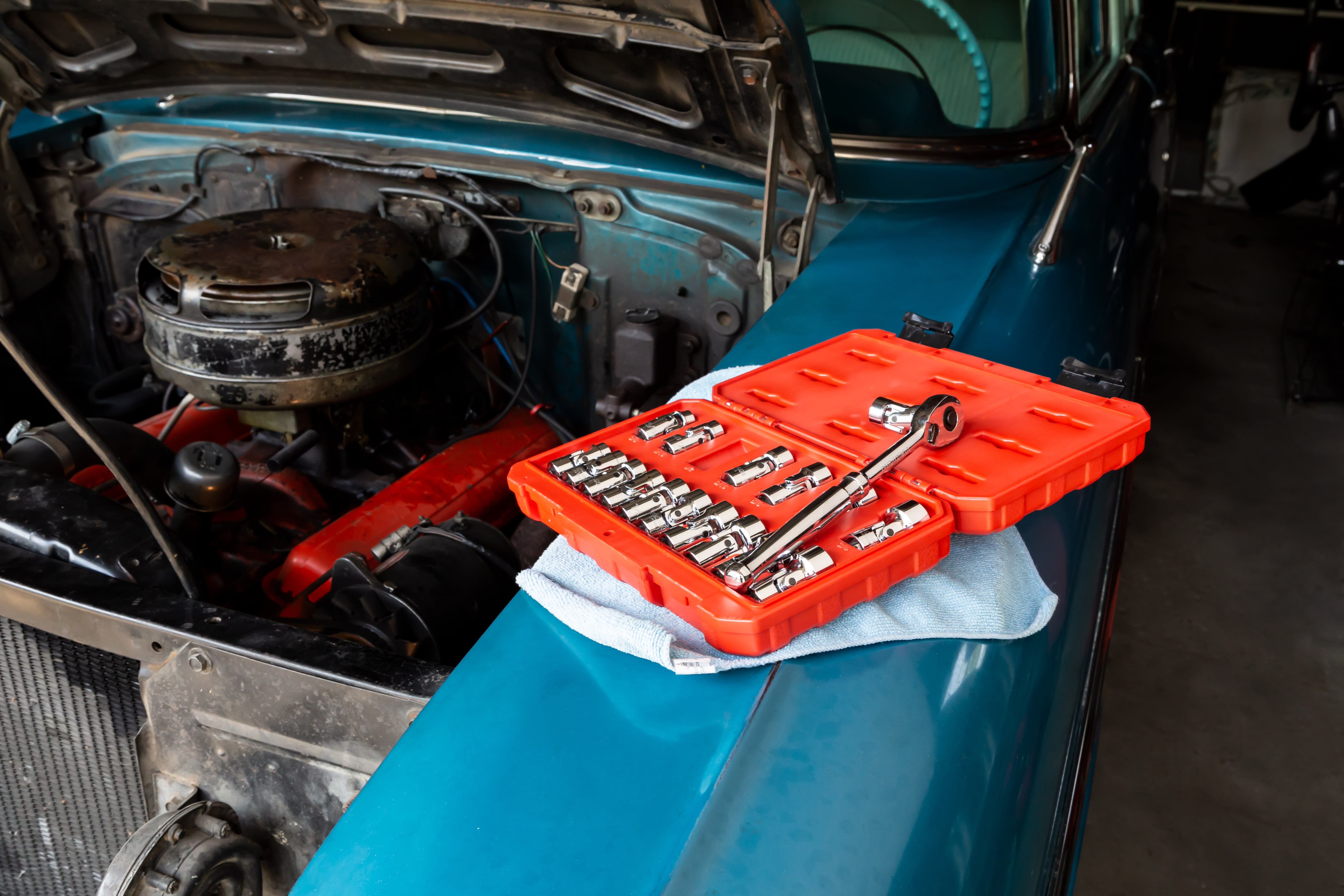 A vintage blue car with its engine hood open and a set of wrenches next to the engine.