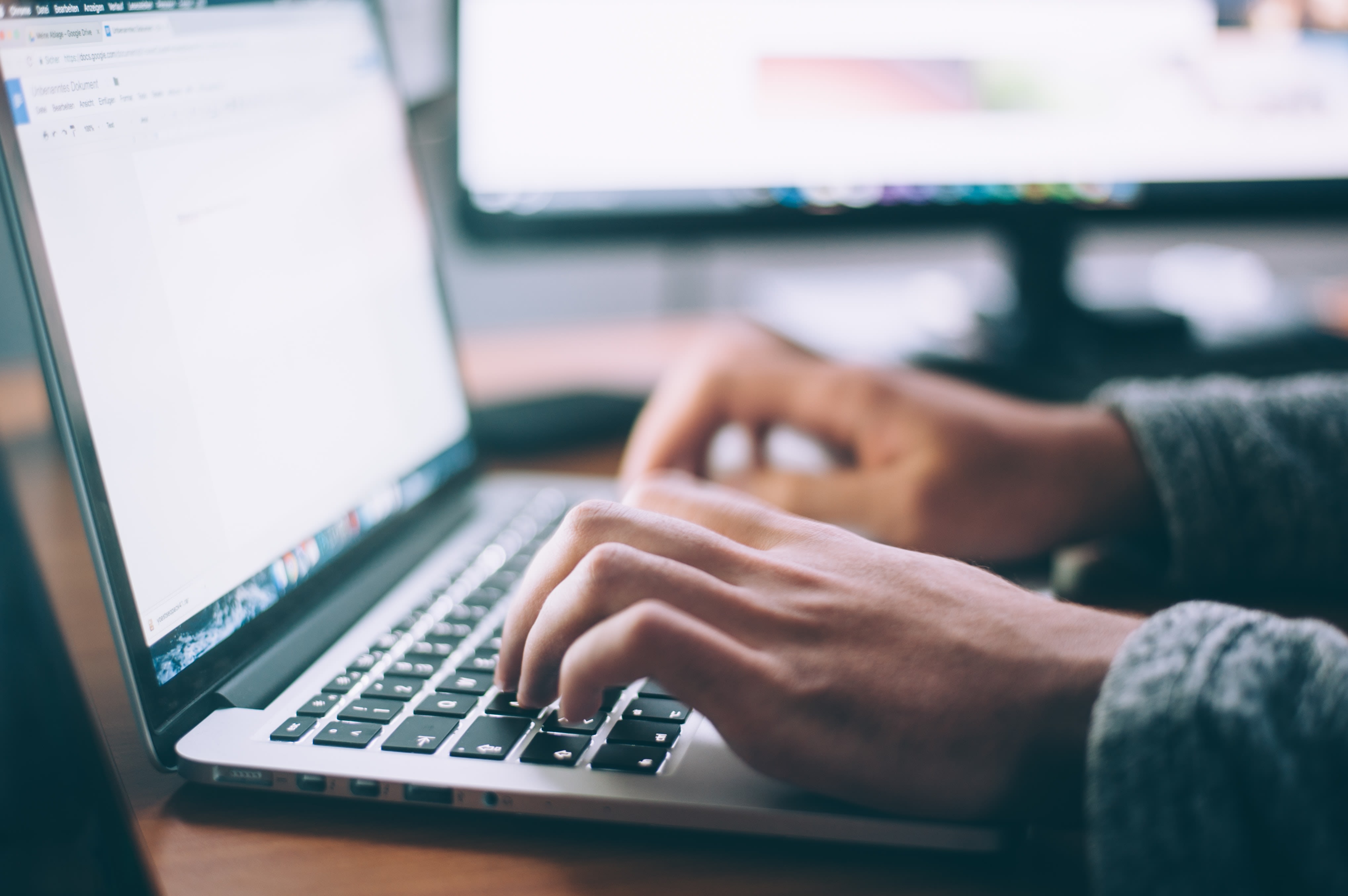 A person's hands typing on a MacBook laptop.