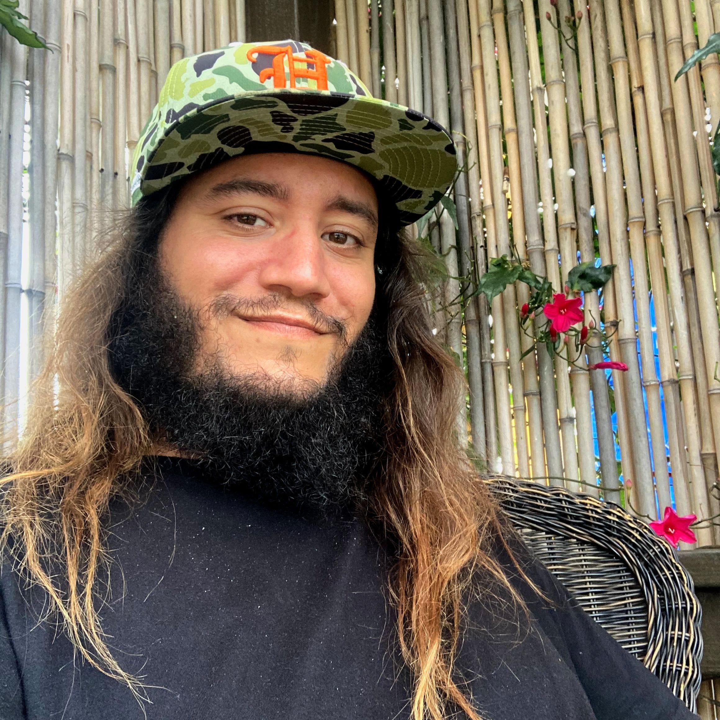 A portrait of Vinnie wearing a camo cap against a bamboo backdrop