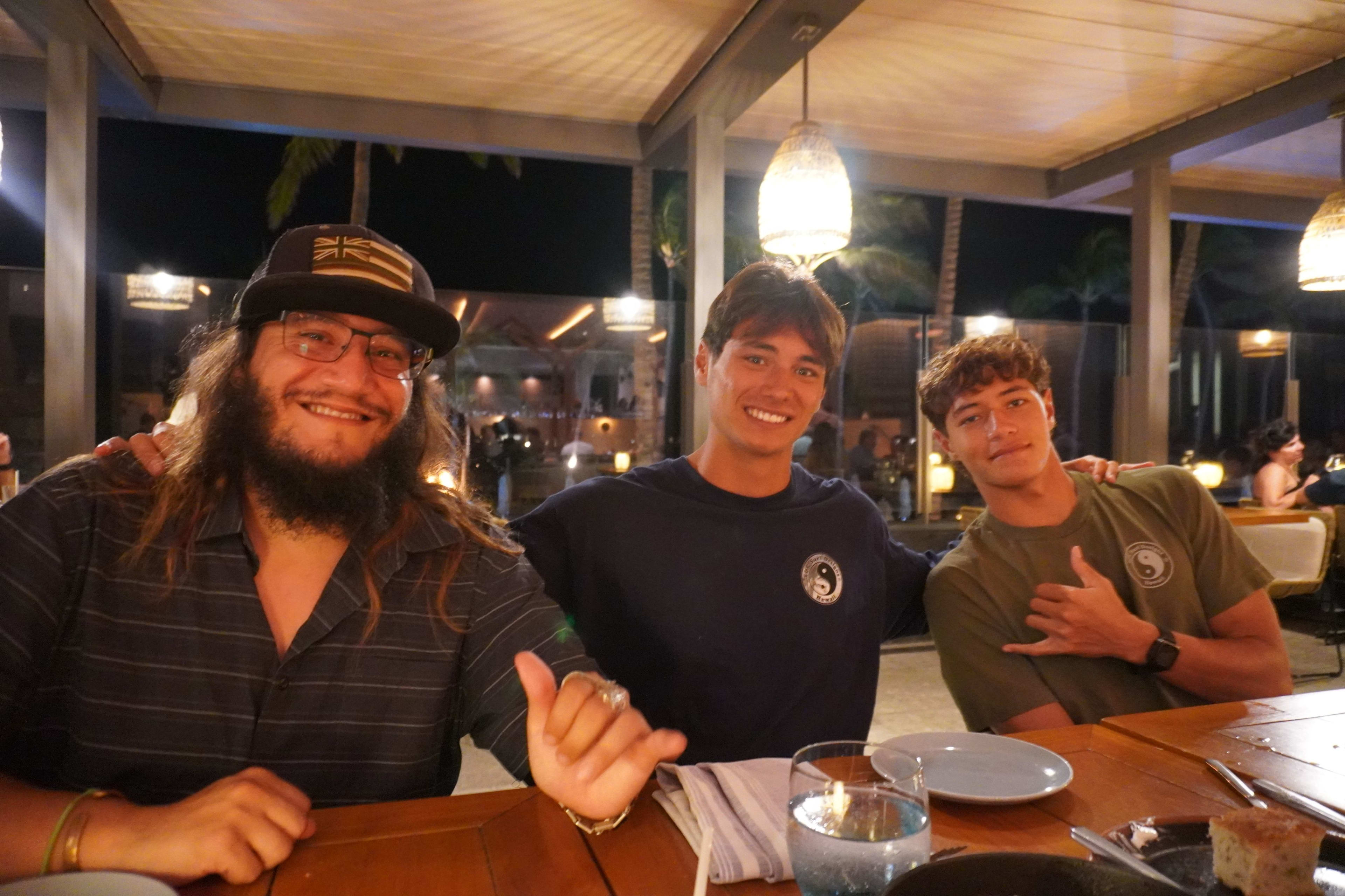 Vinnie with two friends at a restaurant table, giving shaka