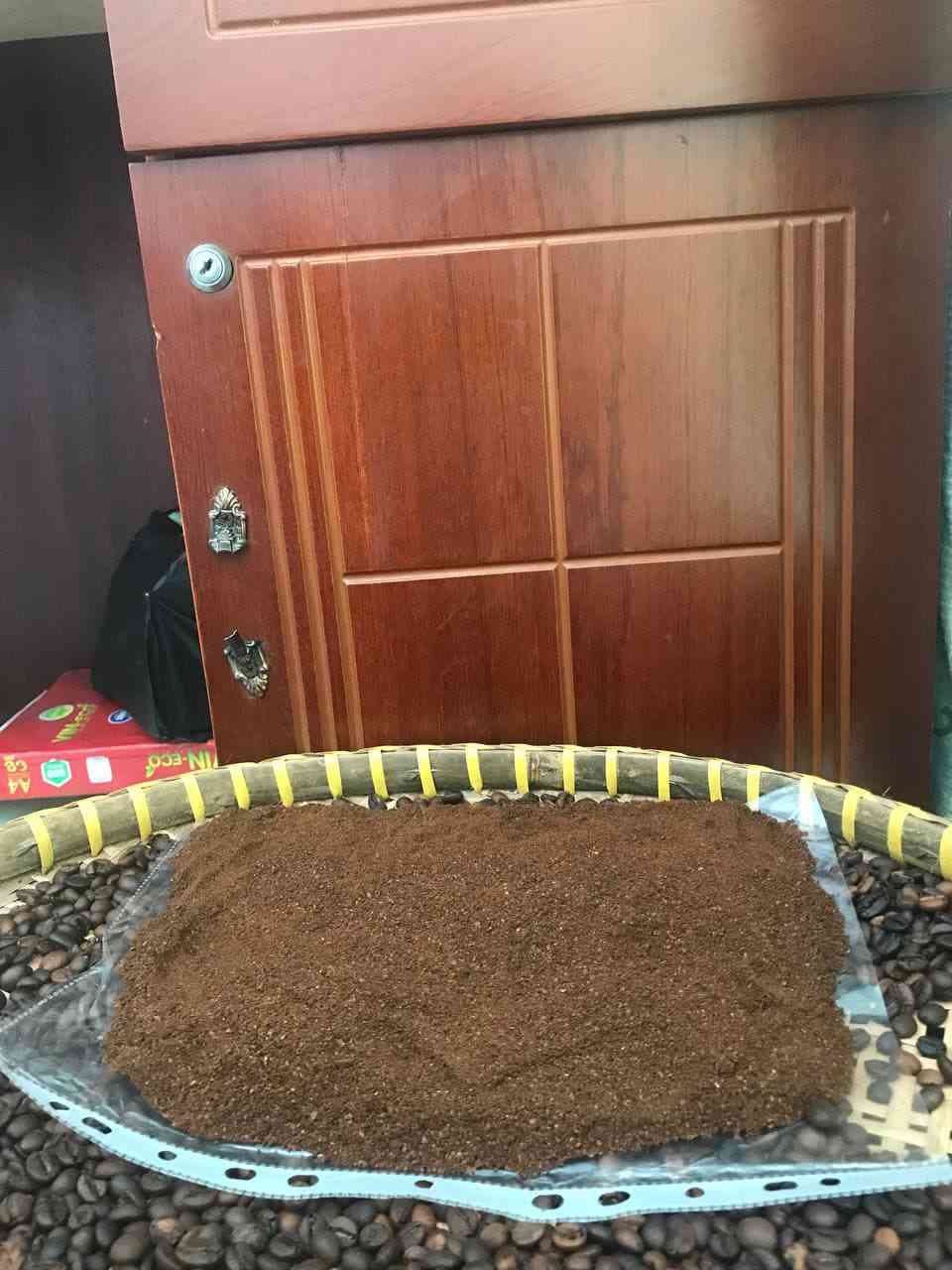 Bột cà phê dàn thành mảng lớn trên khay tre, có hạt rang xung quanh.