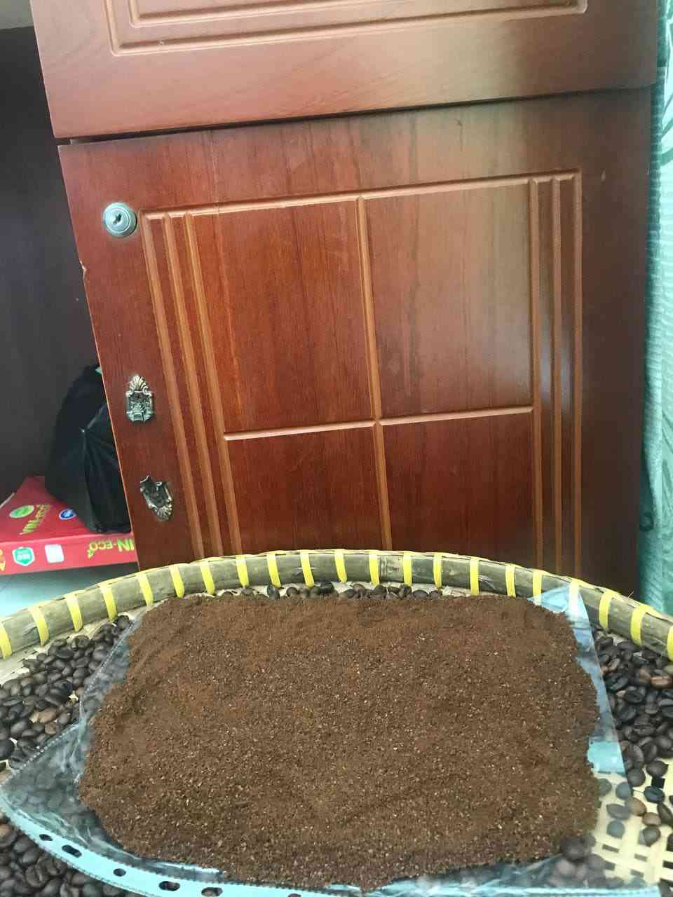 Mảng bột cà phê dàn phẳng trên khay tre, hạt rang ở viền.