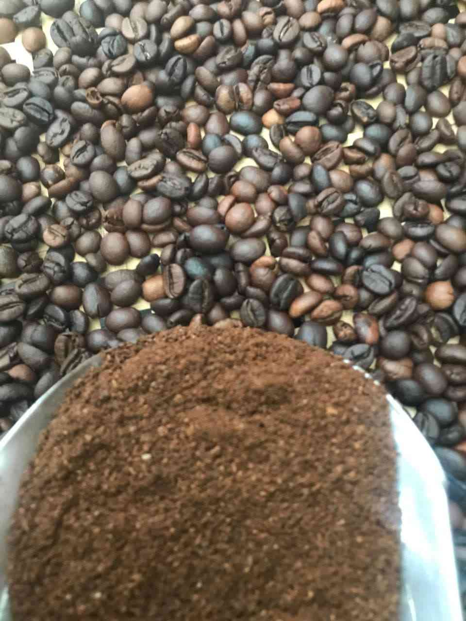 Muỗng/bát chứa bột cà phê ở tiền cảnh trước lớp hạt rang