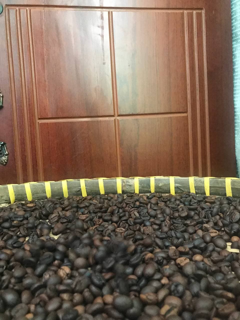 Hạt cà phê rang xếp thành chữ A, mẹt tre nhìn gần; nền phía sau có sàn sáng