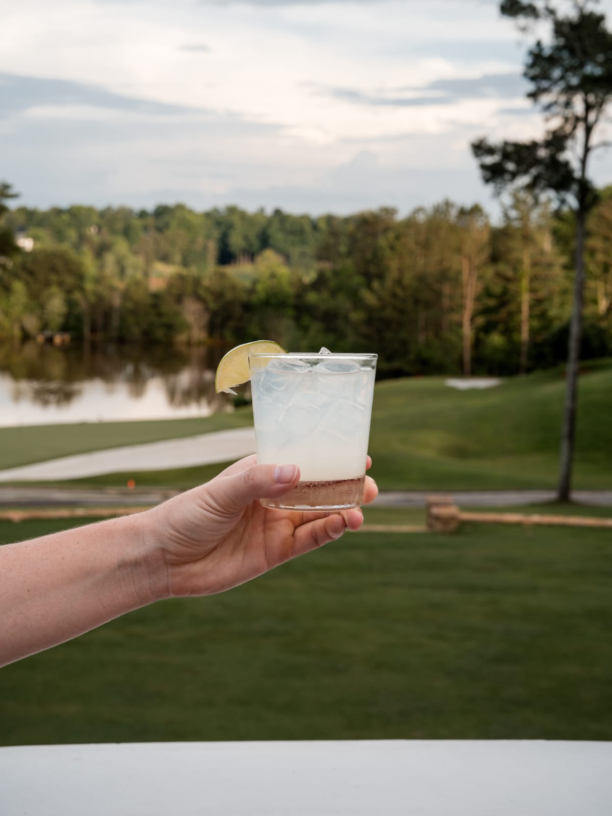 A guest holding an Astral cocktail out over the golf course