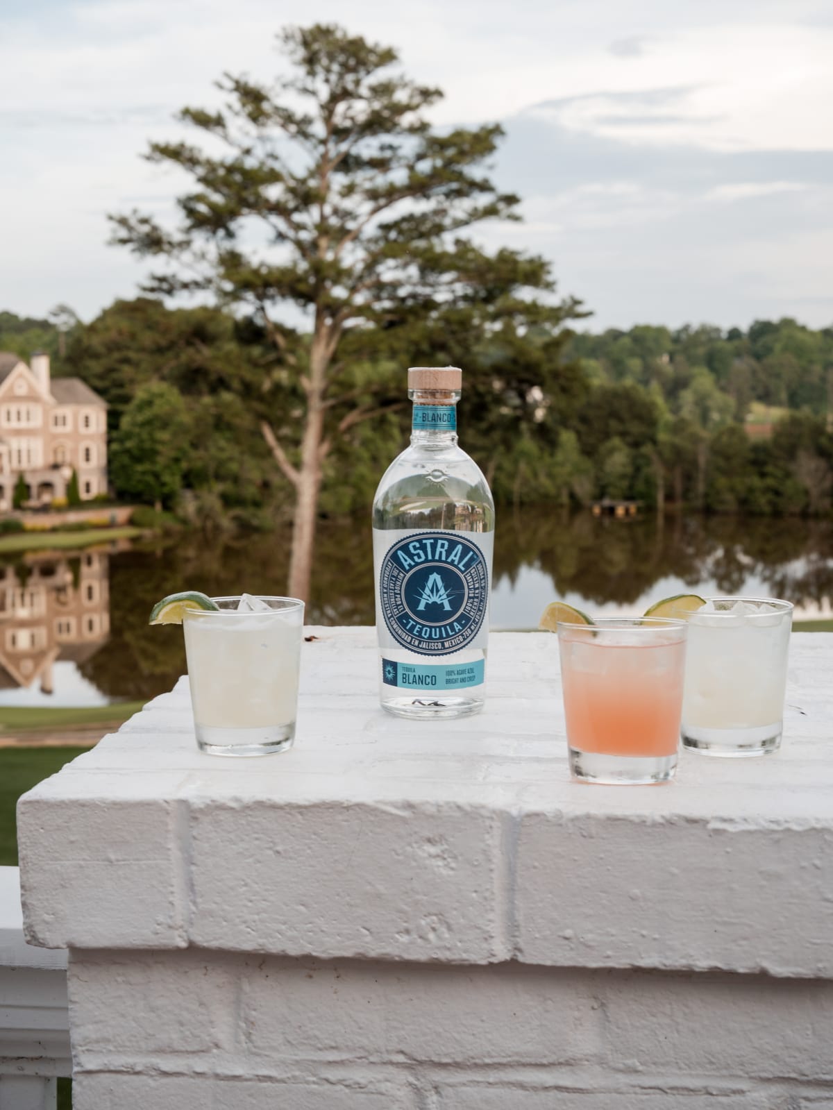 Astral bottle and three cocktails on a brick ledge above the lake