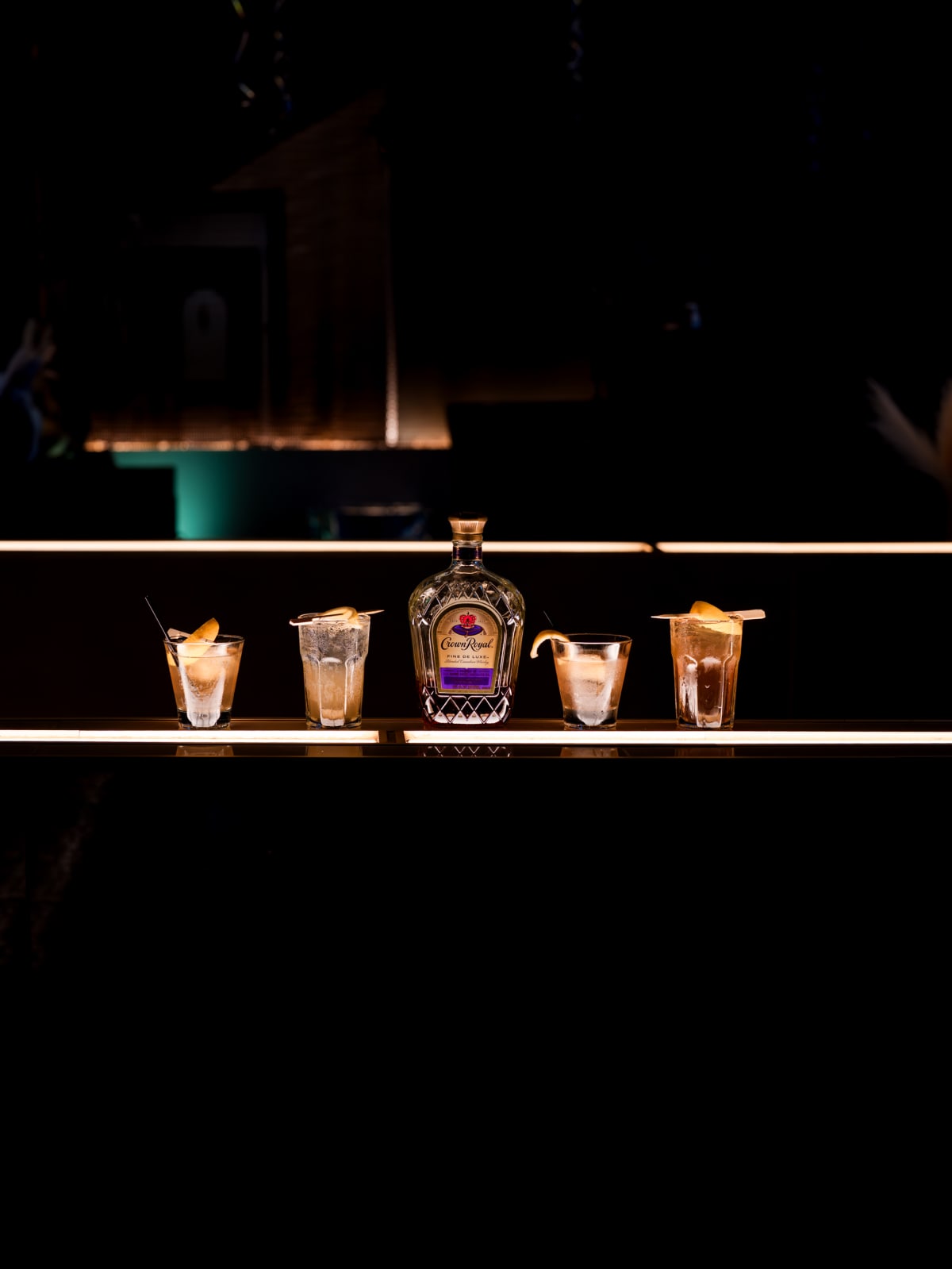 Crown Royal and a row of cocktails along a backlit bar