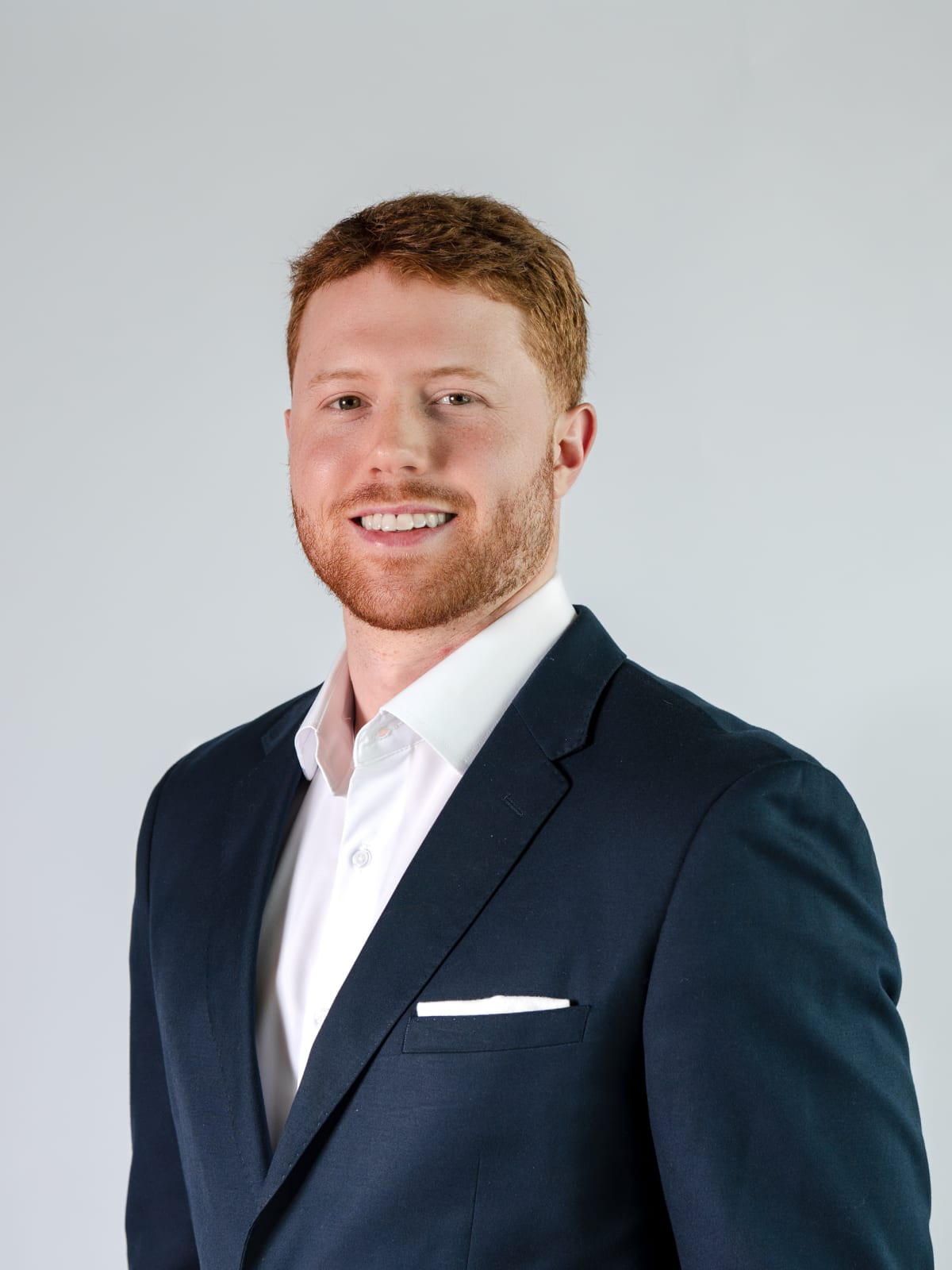 Headshot in a navy suit against a soft grey wall