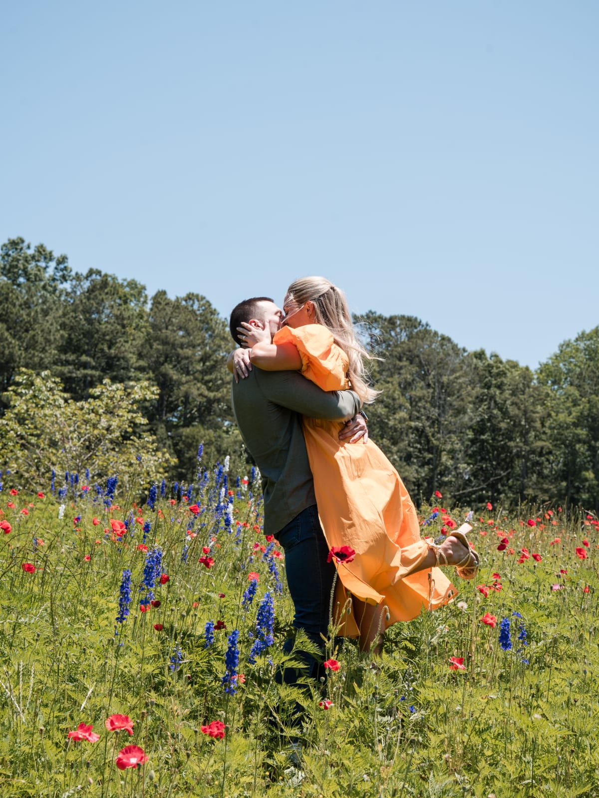 JP lifting Hartley in a field of wildflowers just after she said yes