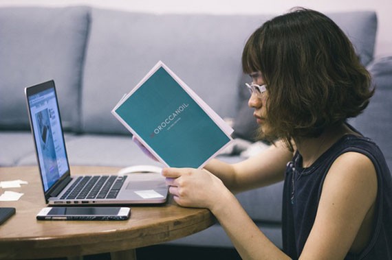 Wanita berambut pendek sedang membaca buku disamping laptop