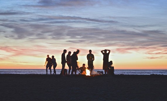 Sekelompok orang membuat api unggun di pantai saat senja
