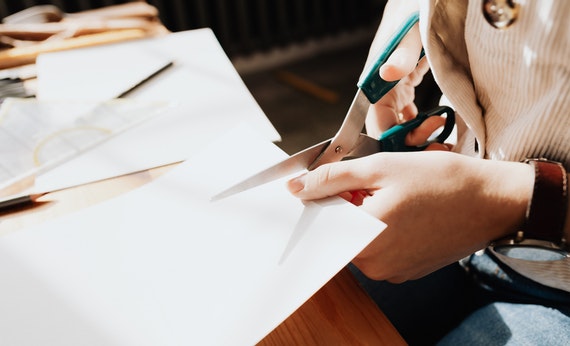 Unrecognizable young craftswoman cutting paper sheet on