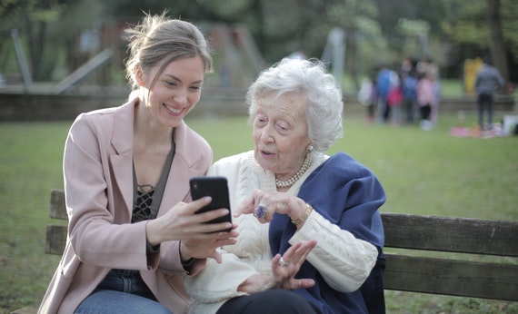 Cheerful senior mother and adult daughter using smartphone