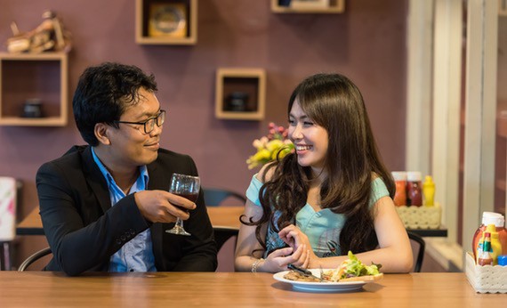 Pria yang memakai jas warna hitam dan wanita yang memakai gaun warna turquoise sedang bekencan di cafe
