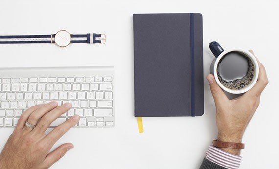 Buku, secangkir kopi, dan keyboard pc diatas meja putih