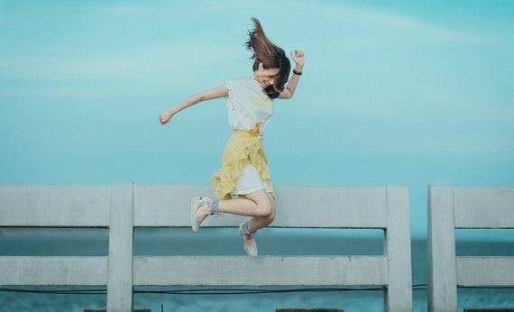 Perempuan memakai dress putih sedang melompat