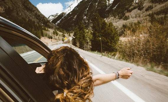 Wanita mengendarai mobil sambil mengeluarkan tangan kanan dari jendela mobil