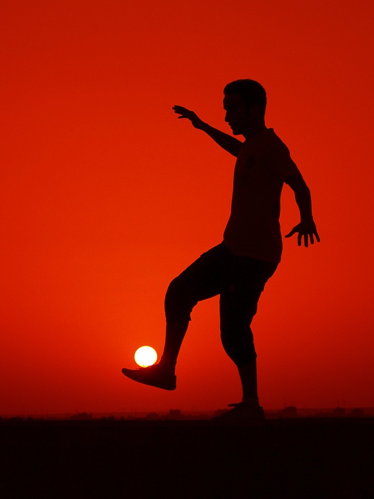 Foto tepat waktu silhouette pria bermain bola dengan sinar matahari
