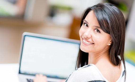Wanita menggunakan laptop sambil menolehkan wajahnya ke belakang