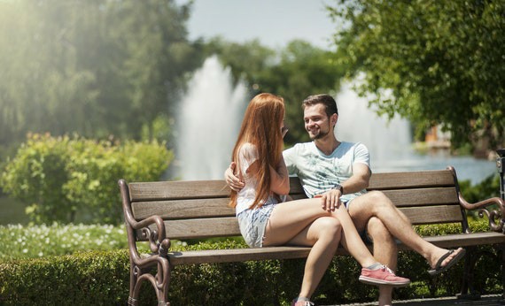 Dua orang jatuh cinta sedang mengobrol di bangku taman dengan latar belakang air mancur