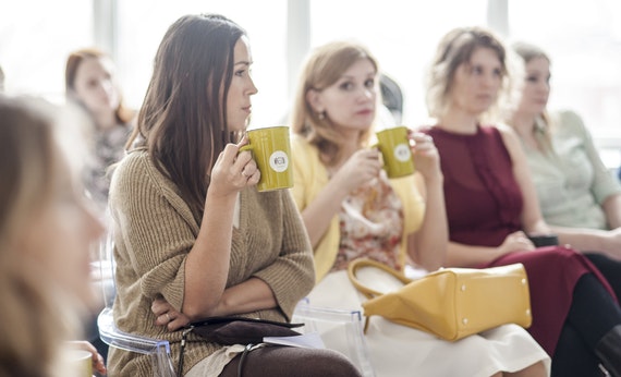 Tiga wanita memegang cangkir sedang duduk di acara seminar
