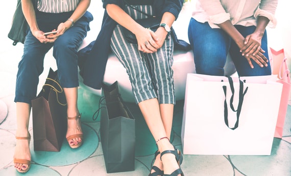 Tiga wanita sedang berbelanja di mall sambil membaca tas belanja