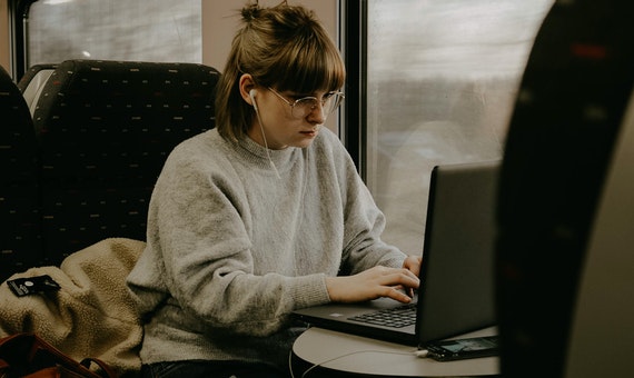 Wanita berkacamata sedang membuka laptop di dalam kereta