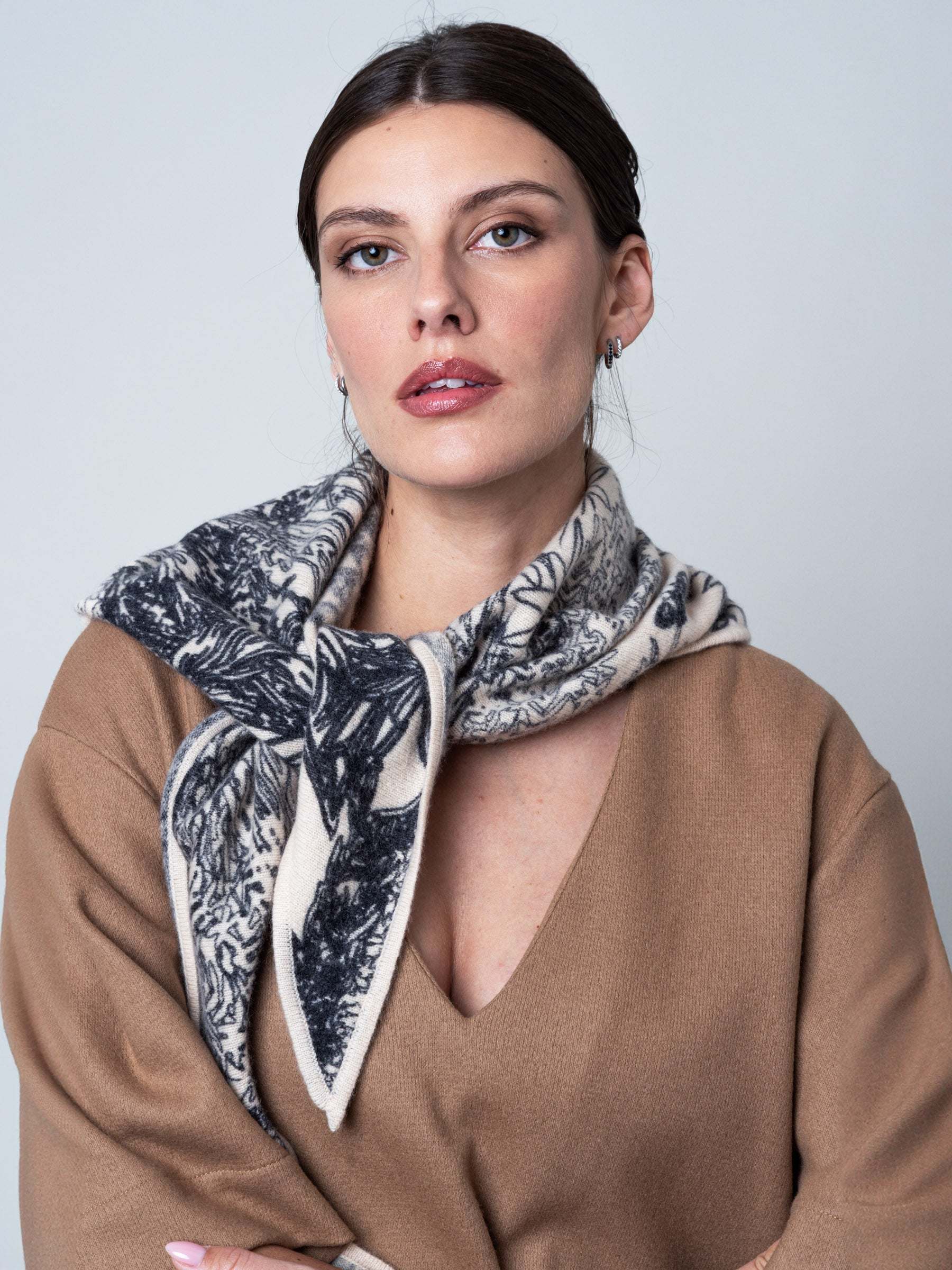 Model wearing the Petrusse Maya cashmere triangle scarf knotted at the neck over a camel sweater