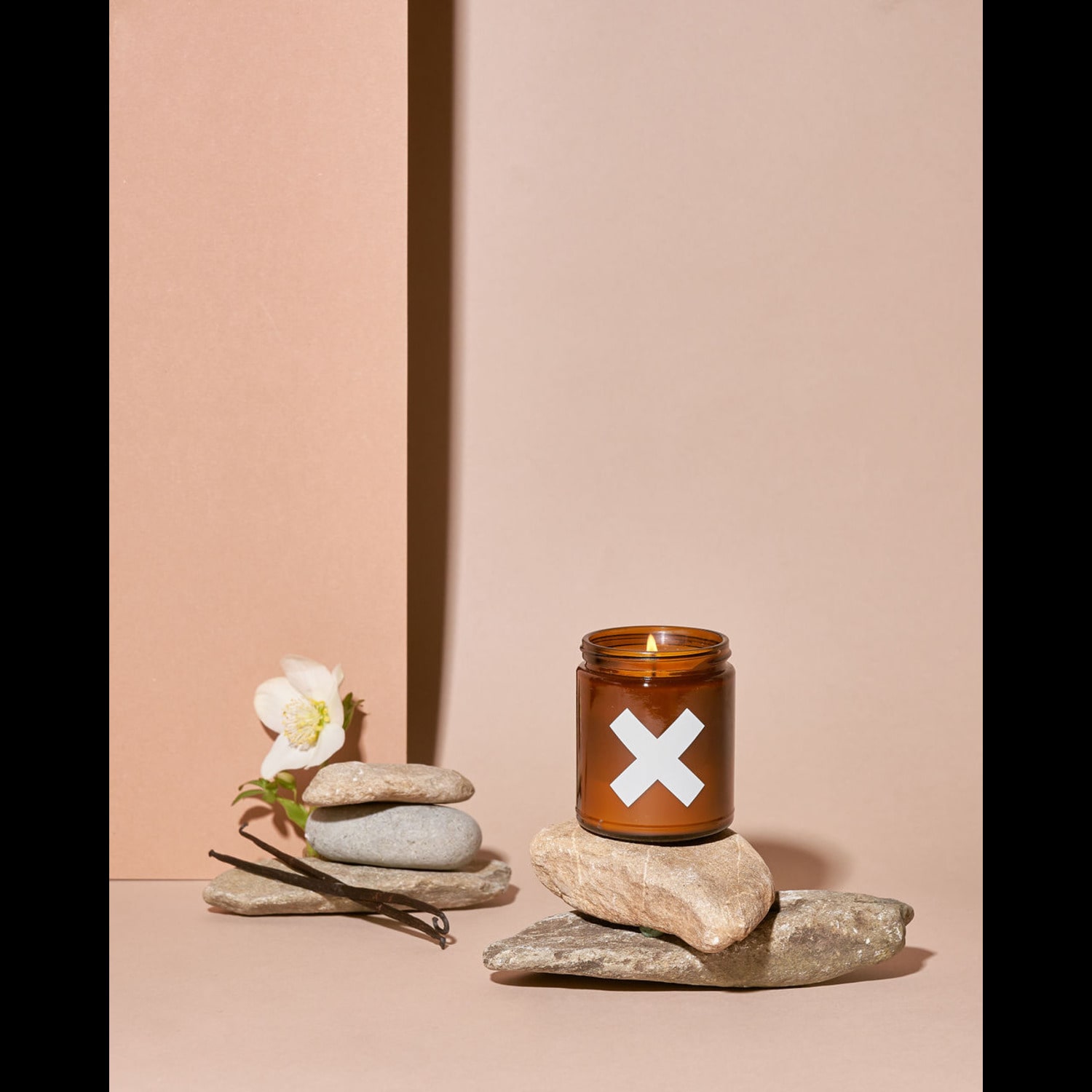 Wax Buffalo Sweet Tobacco soy candle in an amber glass jar on stacked stones with a white flower